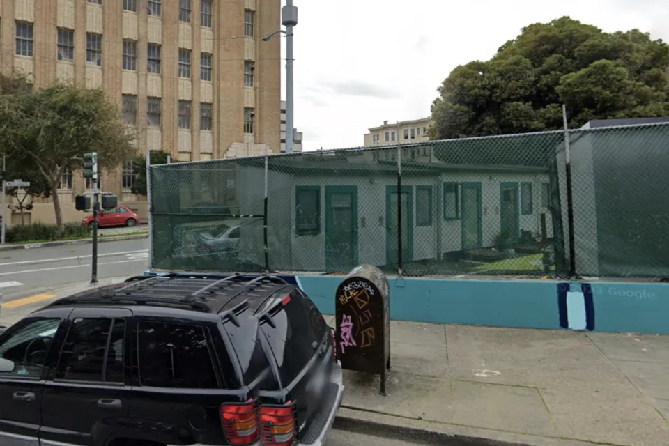 Google street view of tiny home village behind see-through green fence at 33 Gough St. in San Francisco with brick building in background